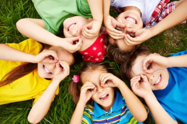 groupe d'enfants allongés en cercle sur l'herbe entourant leurs yeux avec les mains pour former des lunettes