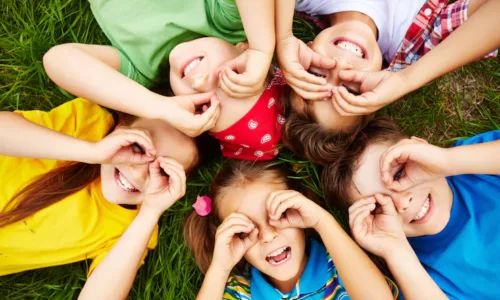 groupe d'enfants allongés en cercle sur l'herbe entourant leurs yeux avec les mains pour former des lunettes